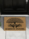 18x24 inch rectangular coir doormat made from natural coconut husk fibers, featuring a bold black print of a stylized tree with branching leaves and intertwined roots forming the shape of protective hands. Below the tree design, the phrase "GUARDED BY ANCESTORS" is printed in large, capitalized serif lettering. The mat has a textured, bristled surface ideal for scraping dirt and moisture from shoes, and a durable construction suited for everyday entryway use. Designed for indoor or outdoor placement, this d
